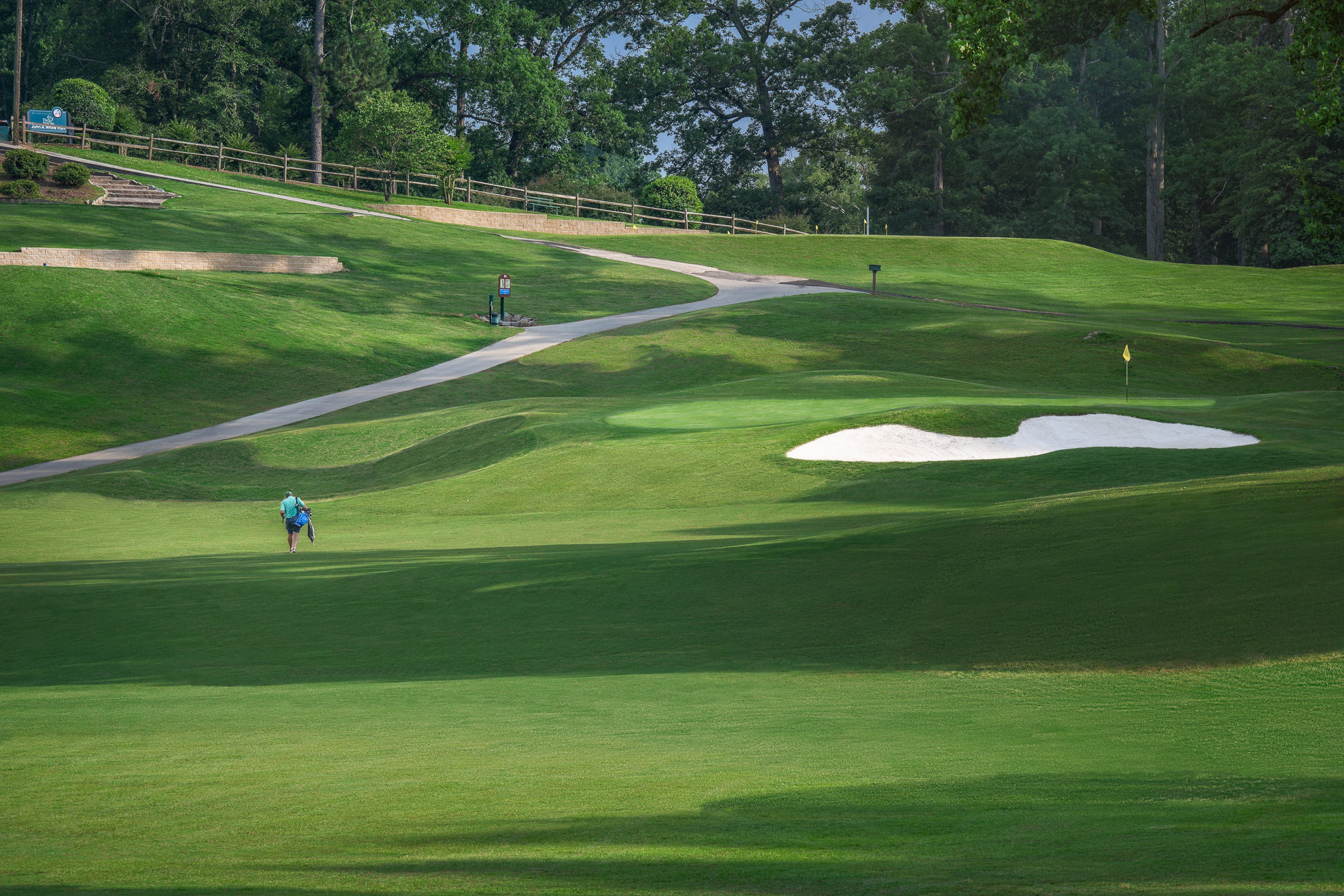 Course greens with sand dunes and cart path leading up a slope 